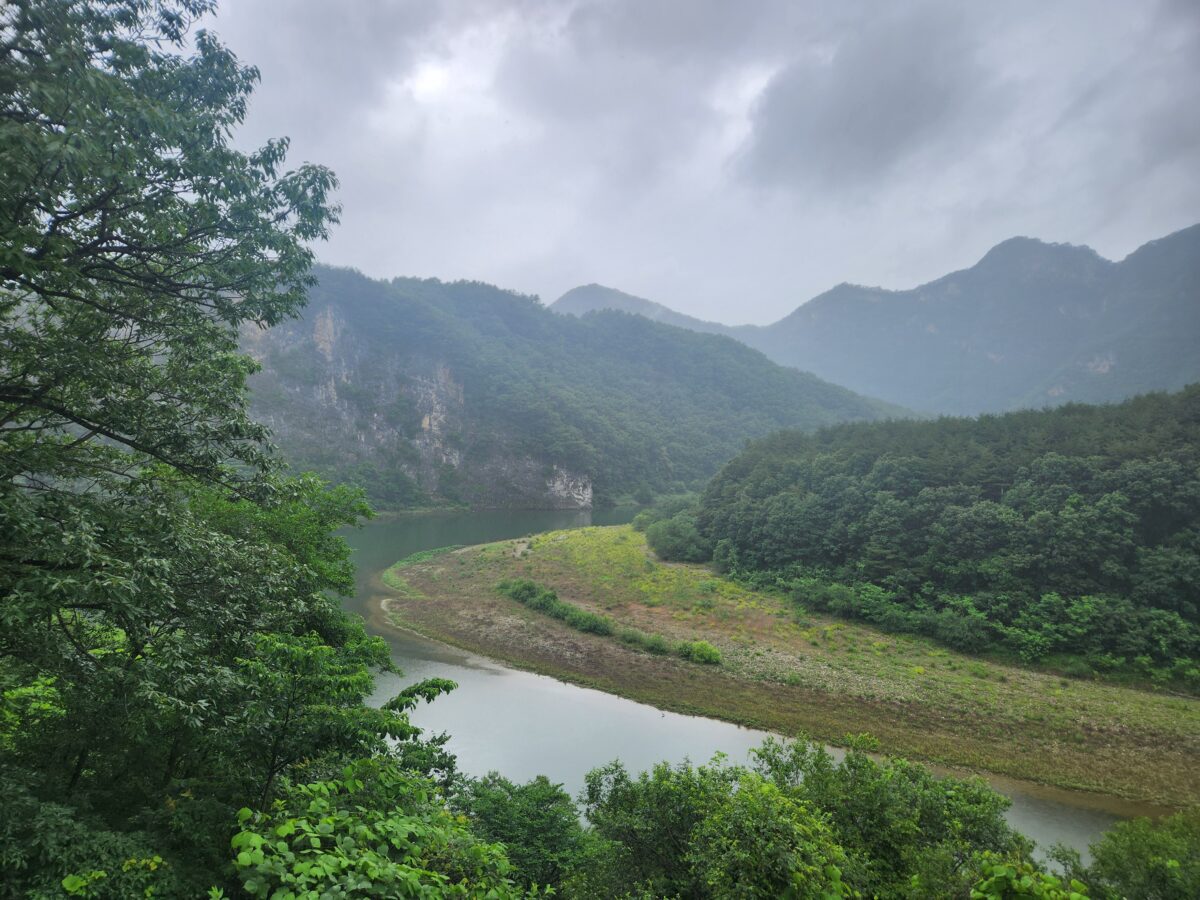 burnout body signals — quiet river valley winding through mountains under cloudy sky
