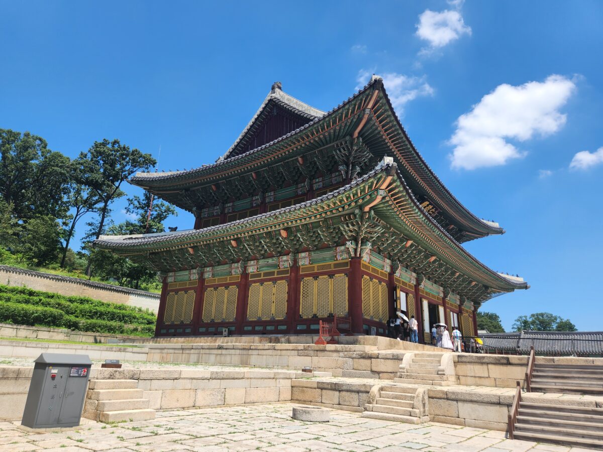 drifting from friends — Korean palace building under blue sky, people walking alone at the entrance