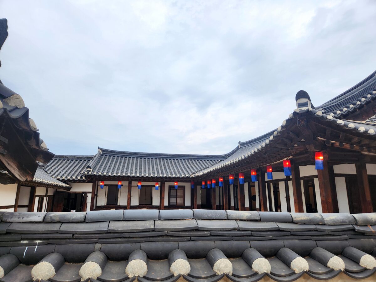 Korean jang philosophy rooted in traditional space — hanok courtyard with tiled roofs and colorful lanterns hanging under an overcast sky