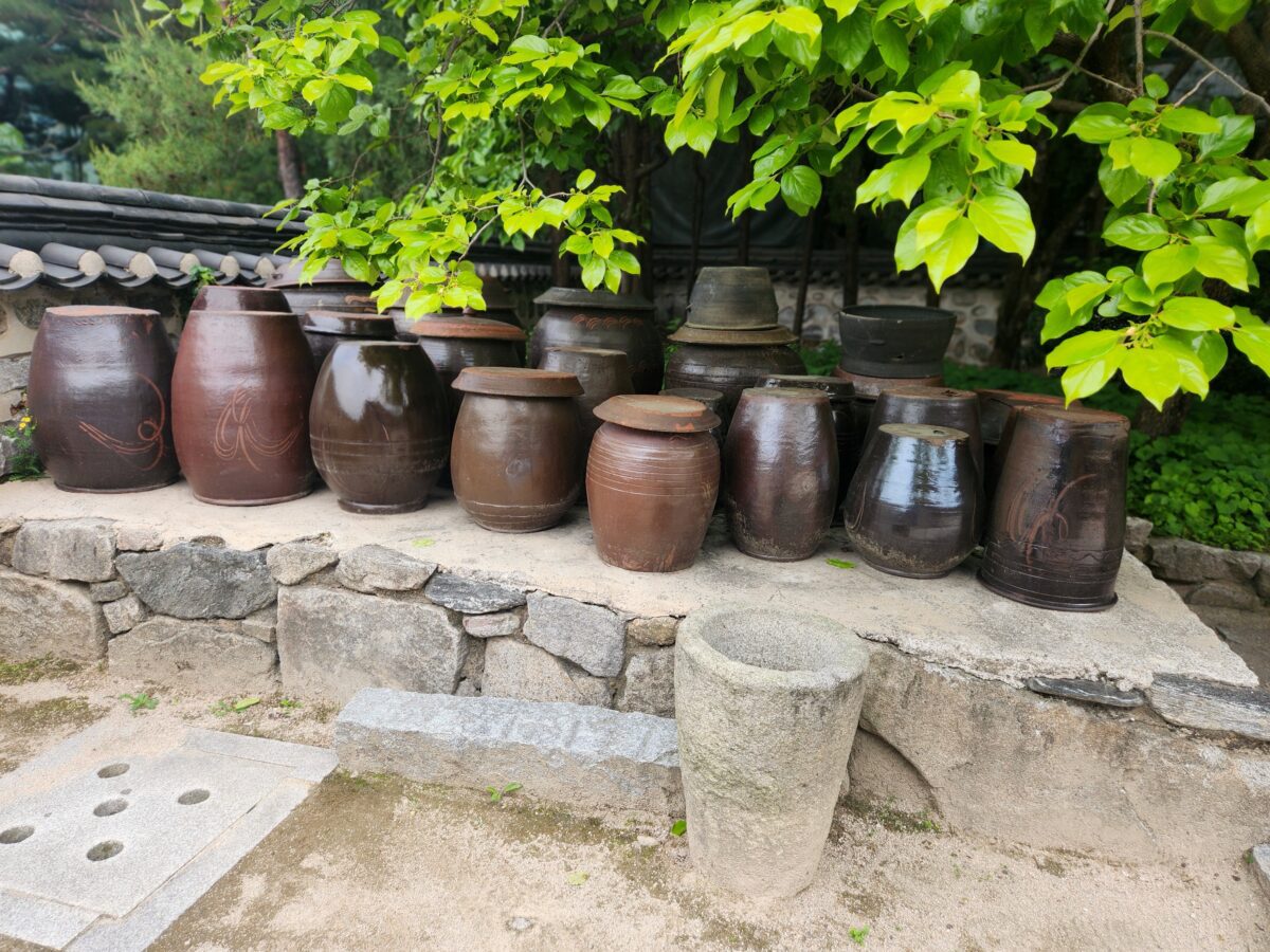 Korean jang fermentation jars at a traditional jangdokdae, arranged on stone under summer trees