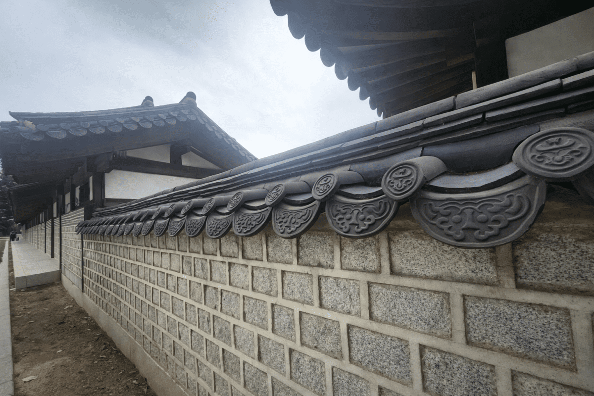 Decorative makse roof tiles along a traditional Korean hanok stone wall under a cloudy sky