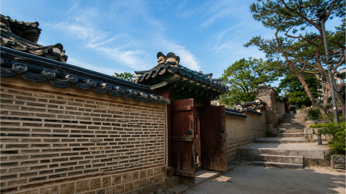 solar return timing — Namsangol Hanok wall with half-open wooden gate and stone steps, same chart different ground conditions, Seoul