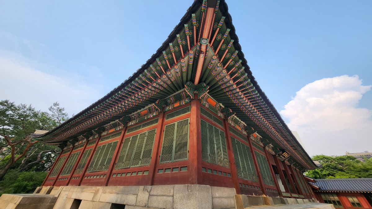 Upward view of a Korean palace roof eave with dancheong patterns against blue sky, anchoring Taegeukgi meaning in tradition.