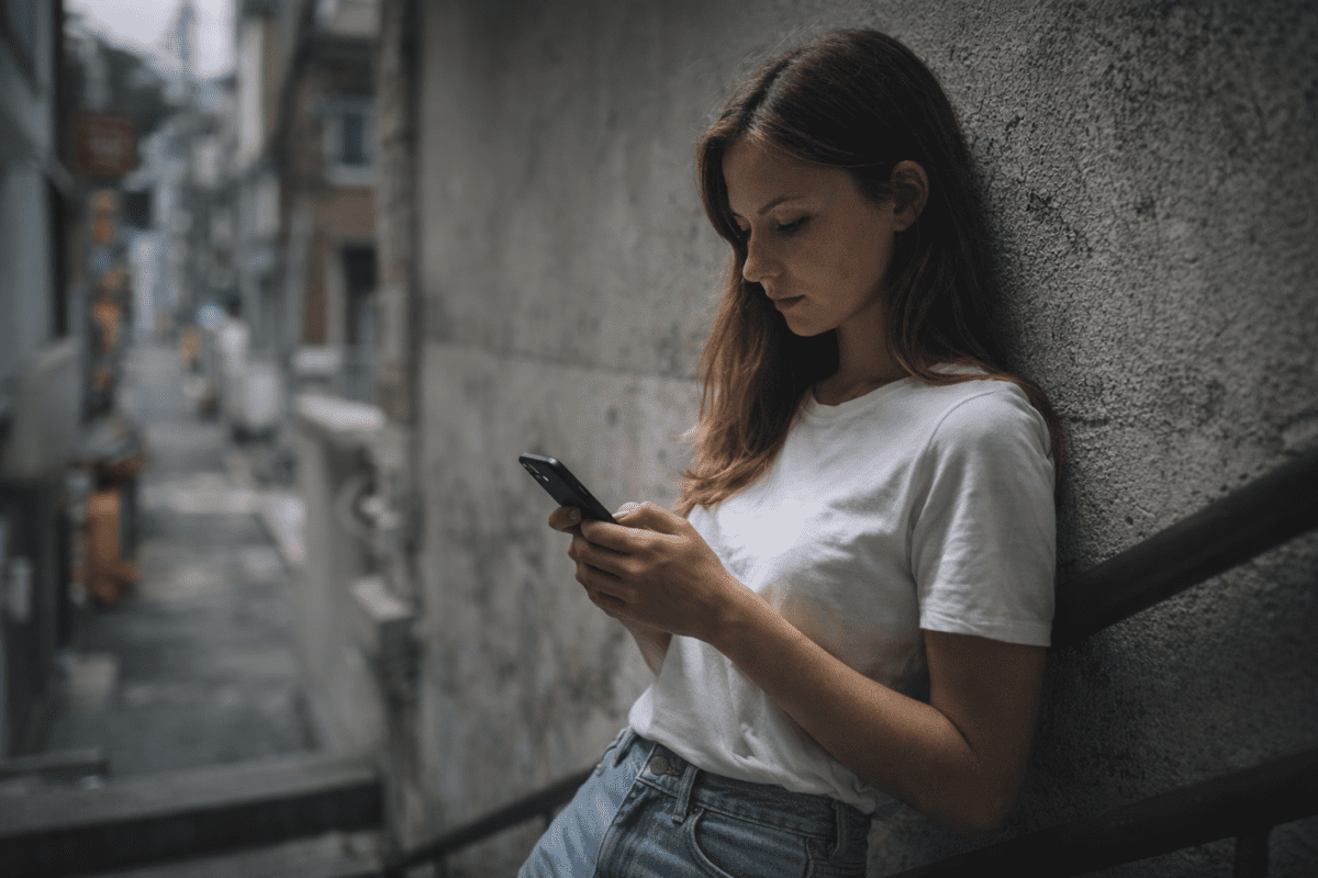 parents expectations and guilt — woman leaning on alley wall looking at phone psychology