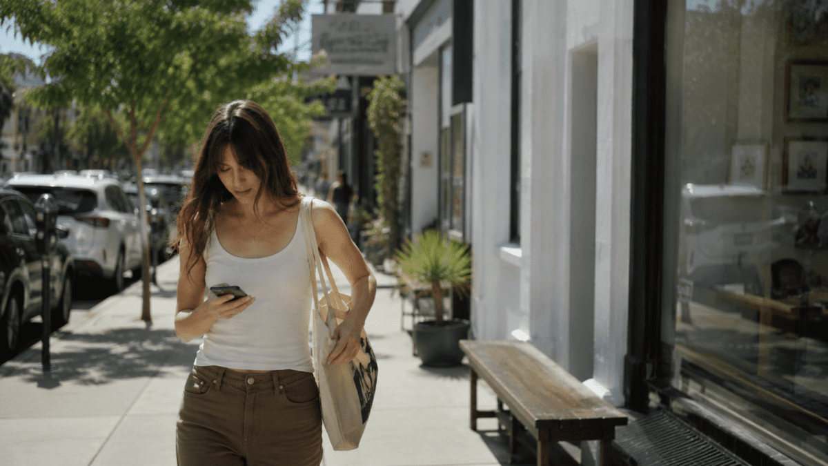 group chat anxiety — woman glancing at her phone while walking down the street