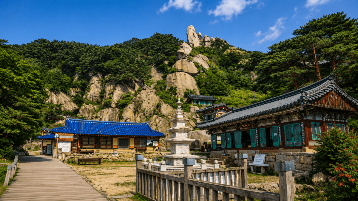 Traditional Korean temple sitting beneath a steep granite peak, ancient stone landscape rising behind it.