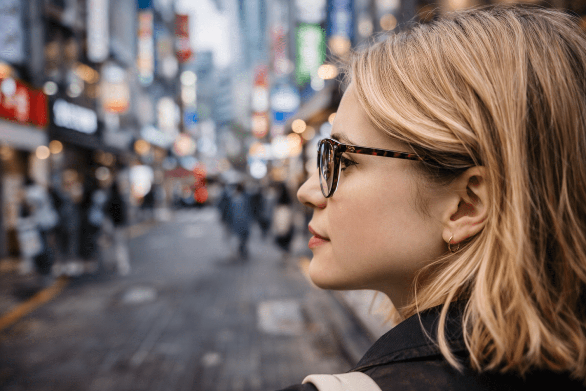 Western woman wearing new glasses on a Seoul street, side profile, city lights bokeh in background, buying glasses in Korea