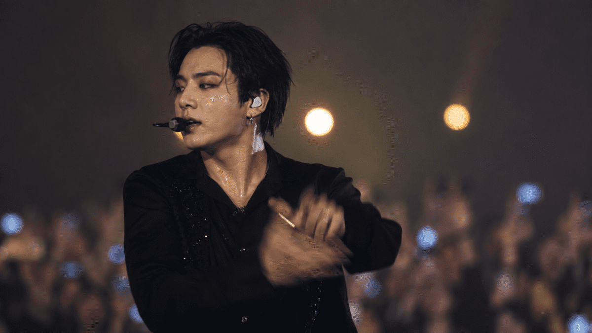 Korean masculinity redefined — male performer in dark stage lighting singing into a microphone before a cheering crowd