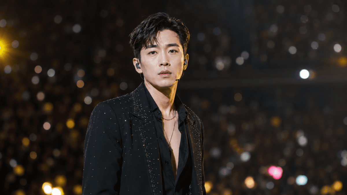 Korean male idol performing on stage with polished makeup, styled hair, and a black outfit, highlighting modern Korean men's beauty and entertainment culture.