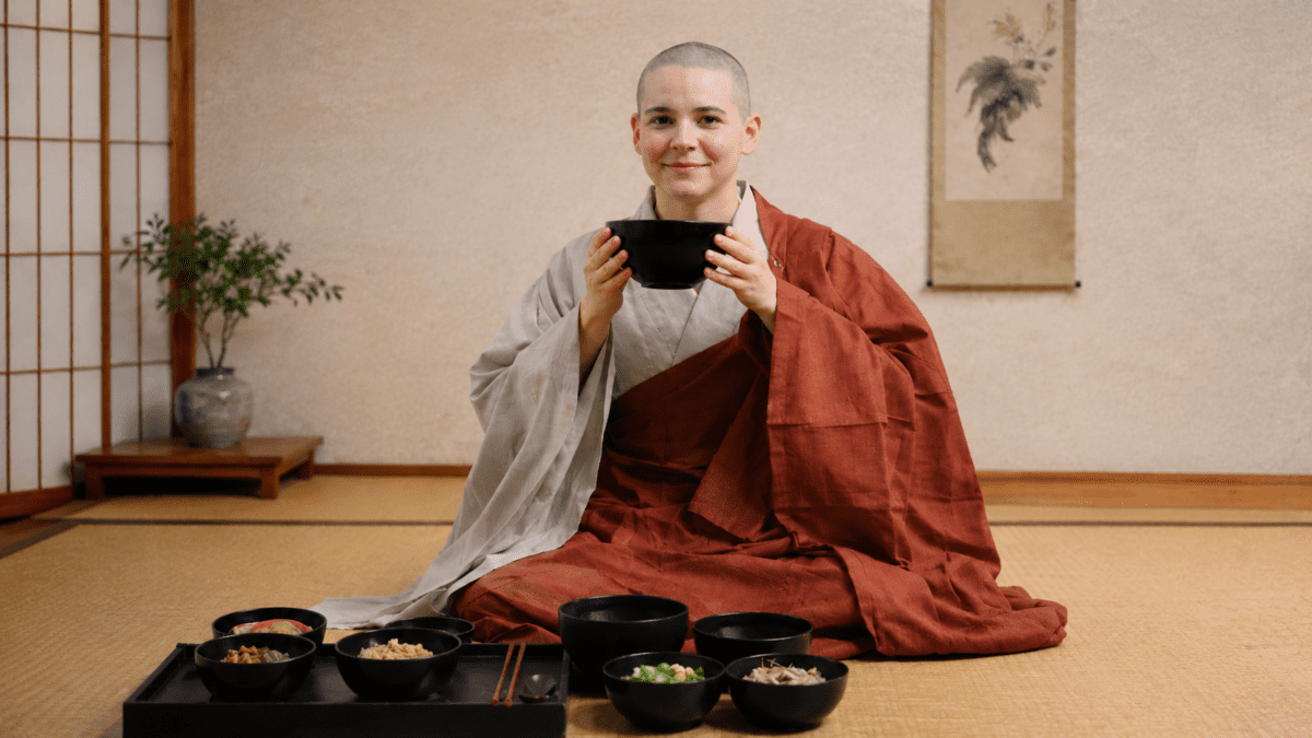 A monk holds a black bowl before a temple meal, side dishes laid out — Korean temple food built without garlic, onion, or shortcuts.