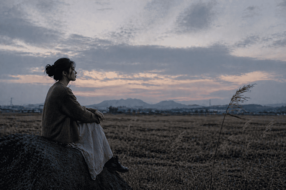 late autumn cycle astrology — a young woman sitting on a stone in an empty field at dusk