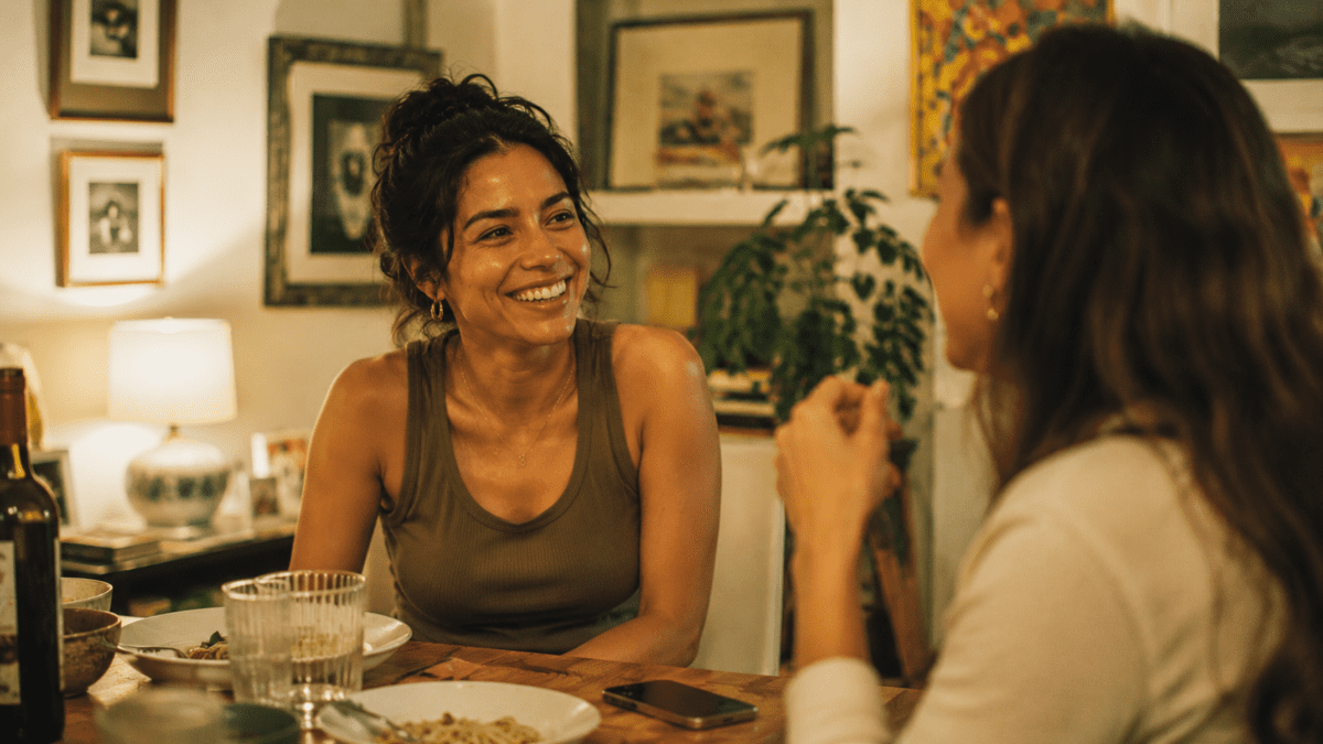 Woman laughing over dinner with a friend, phone face-down on the table, fully somewhere else for once.