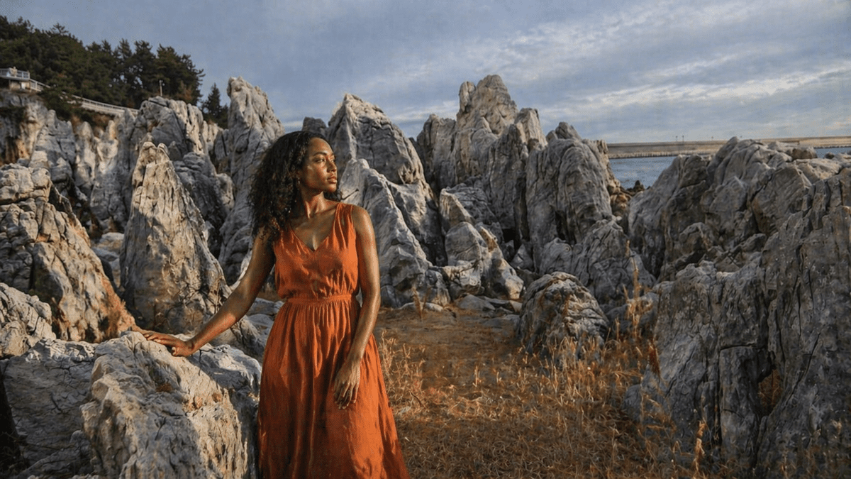 afternoon cycle meaning in astrology — a young woman standing among rugged limestone cliffs by the sea in late afternoon light