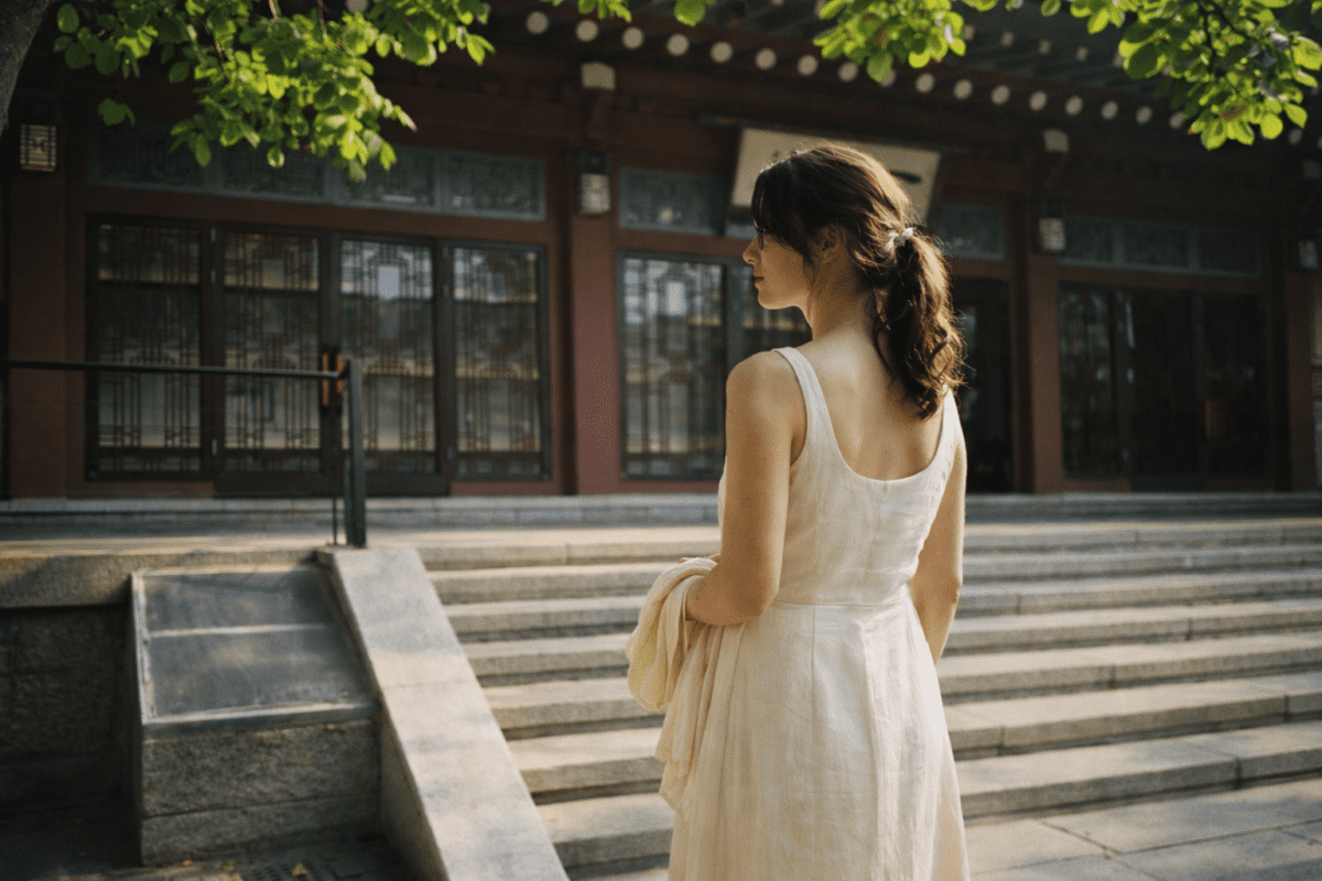 summer solstice meaning in astrology — a young woman standing in bright midday light before a hanok hall