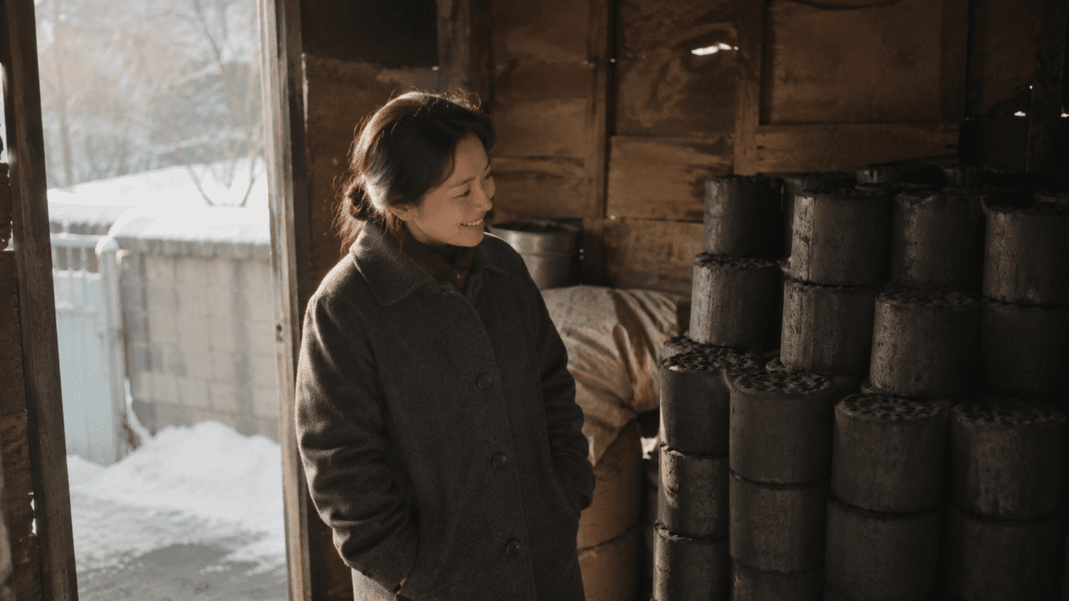 Woman smiling beside stacks of yeontan Korean coal briquette at a snowy storage shed entrance in winter