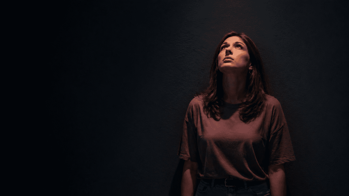 A woman looking upward with a longing, yearning expression against a dark background, representing the anxious attachment style's deep need for connection and fear of being unseen or forgotten.