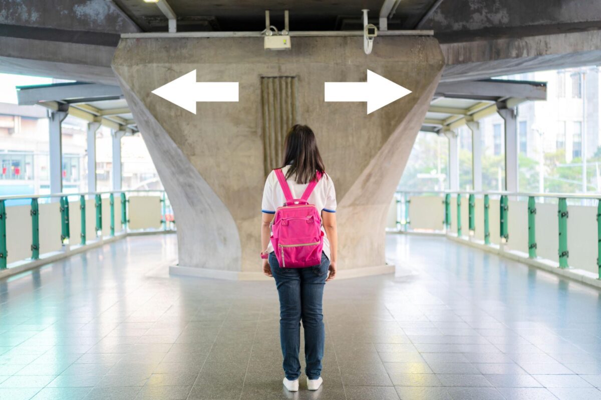 A person standing at a crossroads with arrows pointing in different directions, symbolizing how who you are and where you are determine which path works—showing strength and timing working together in decision-making.