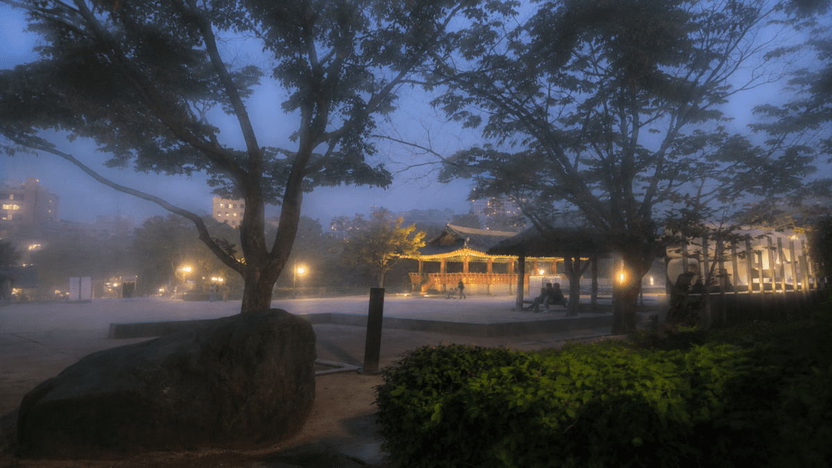 Foggy dawn over a lit Korean pavilion in a park, marking the dragon hour before the day takes shape.
