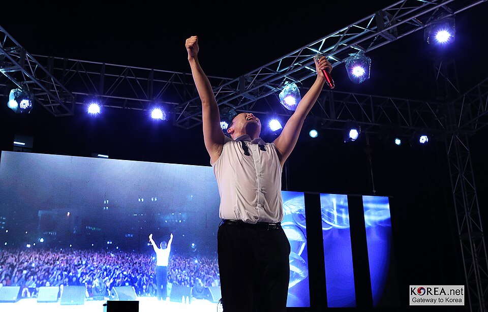 Psy raising his arms during a Gangnam Style performance as the crowd reacts to the global energy of Psy dance