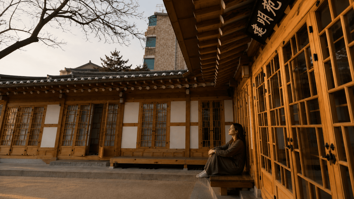 Woman sitting alone in a vast hanok courtyard, surrounded by empty space—visualizing how goalpost shifting creates an endless landscape where no amount of achievement ever feels like arrival.