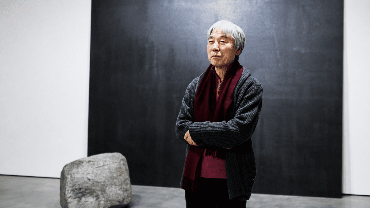 Portrait of Lee Ufan standing before a monochrome canvas reflecting Lee Ufan reduction philosophy