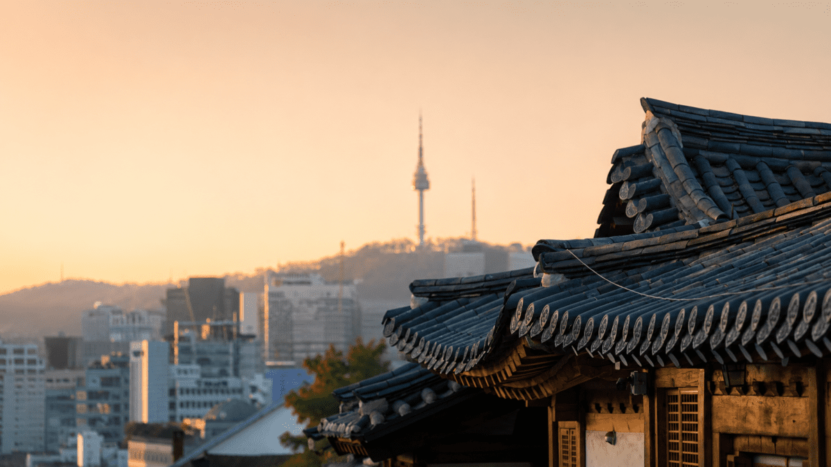 Traditional hanok tile roof overlooking Seoul skyline at golden hour, representing firm boundaries that protect your rhythm from external demands