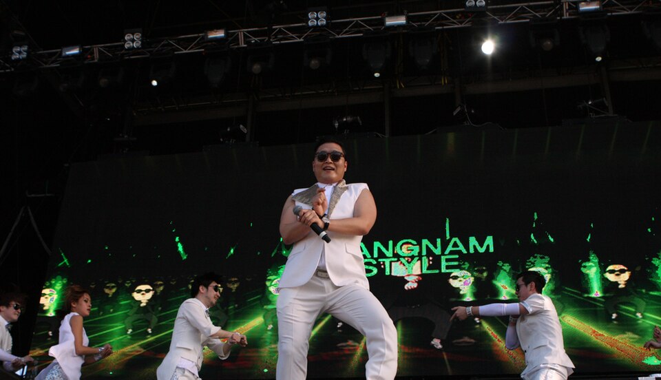 Psy dance performance of Gangnam Style on stage with dancers and green concert visuals