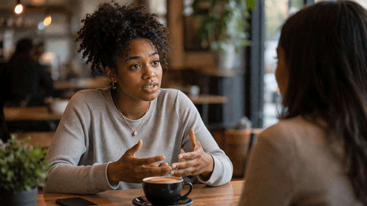 Woman saying sorry first, explaining herself to a friend in a café conversation, gesturing while speaking across the table