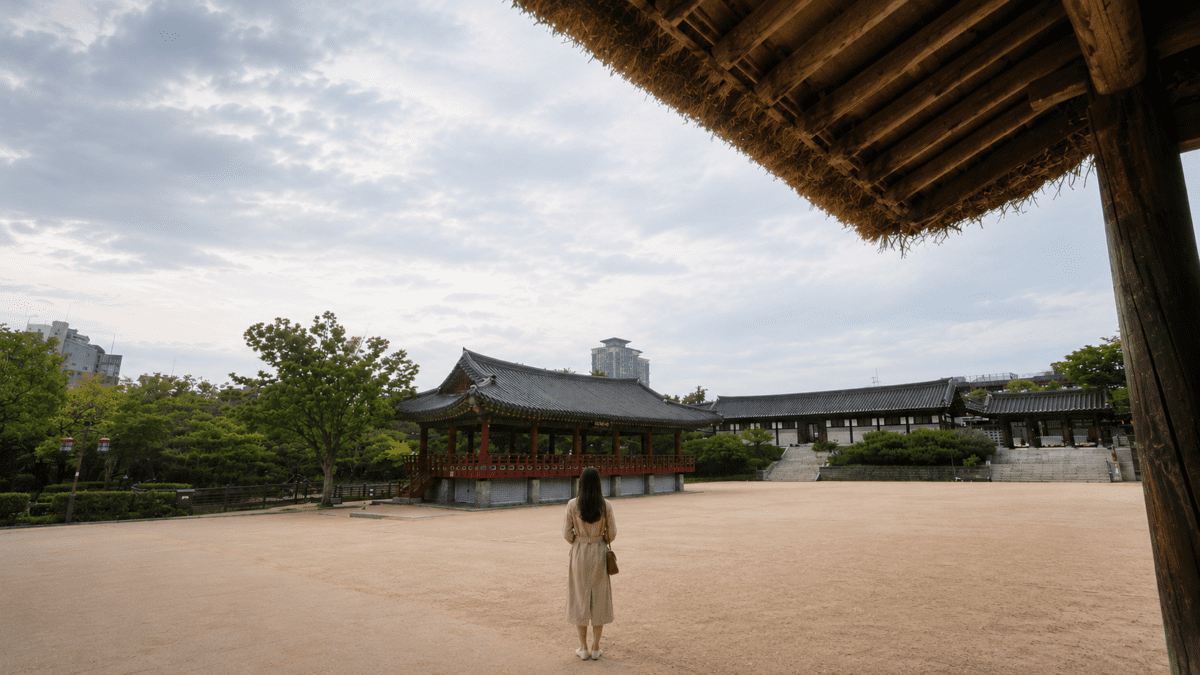Woman stands alone in a quiet courtyard, carrying the weight of silent love beneath a wide evening sky.
