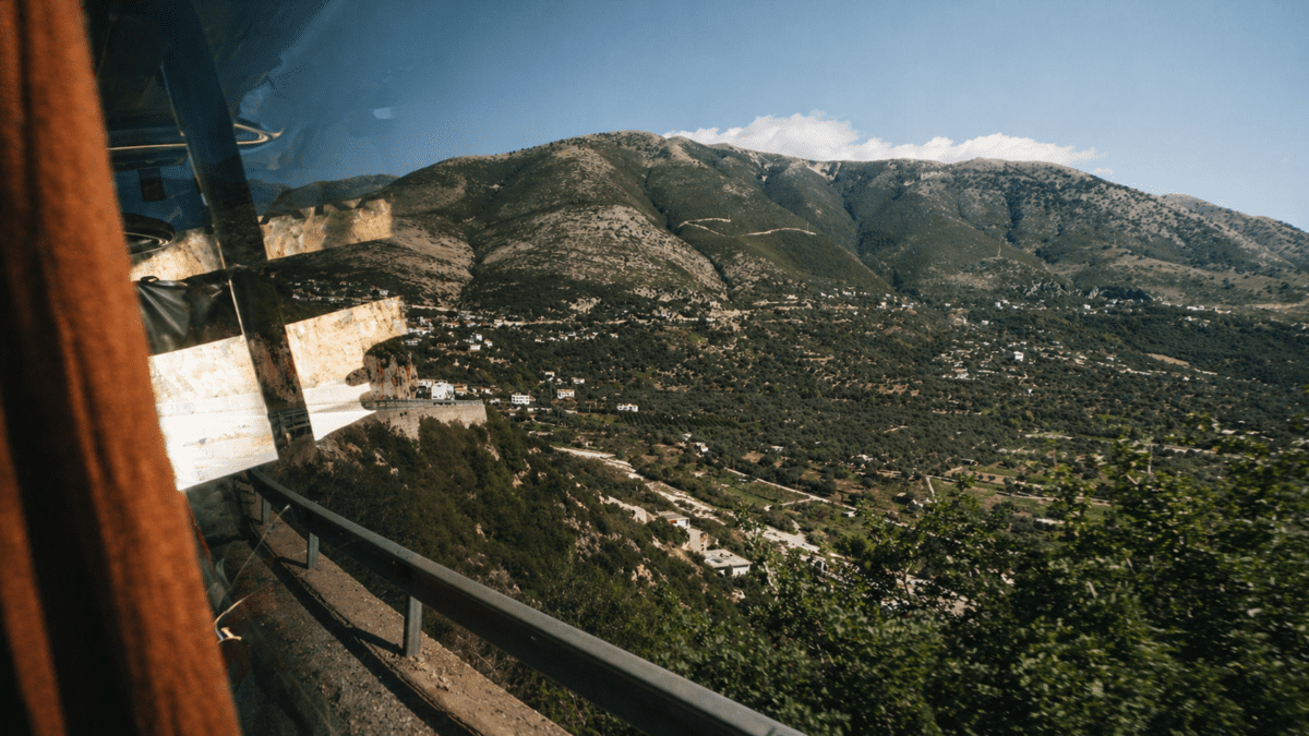 A view of mountains through a bus window as it departs from a temple, representing temple slow food—illustrating the moment when you leave behind the structure and the robes stay, but what travels with you is smaller, more durable, and returns you again.