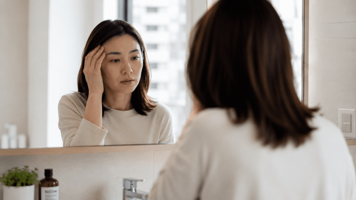 Woman pauses at the mirror, her body quietly signaling what she still hasn't let herself hear.