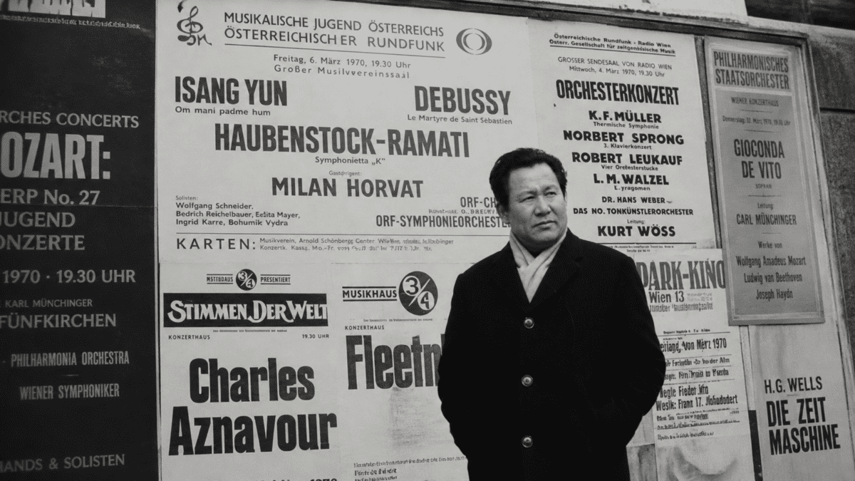 Isang Yun standing before European concert posters, reflecting his international career and political exile era.