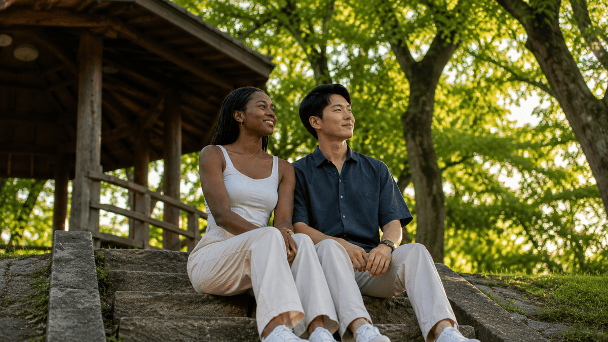 A couple sits on stone steps by a pavilion in Gwanbangjerim, late summer light through the old trees.