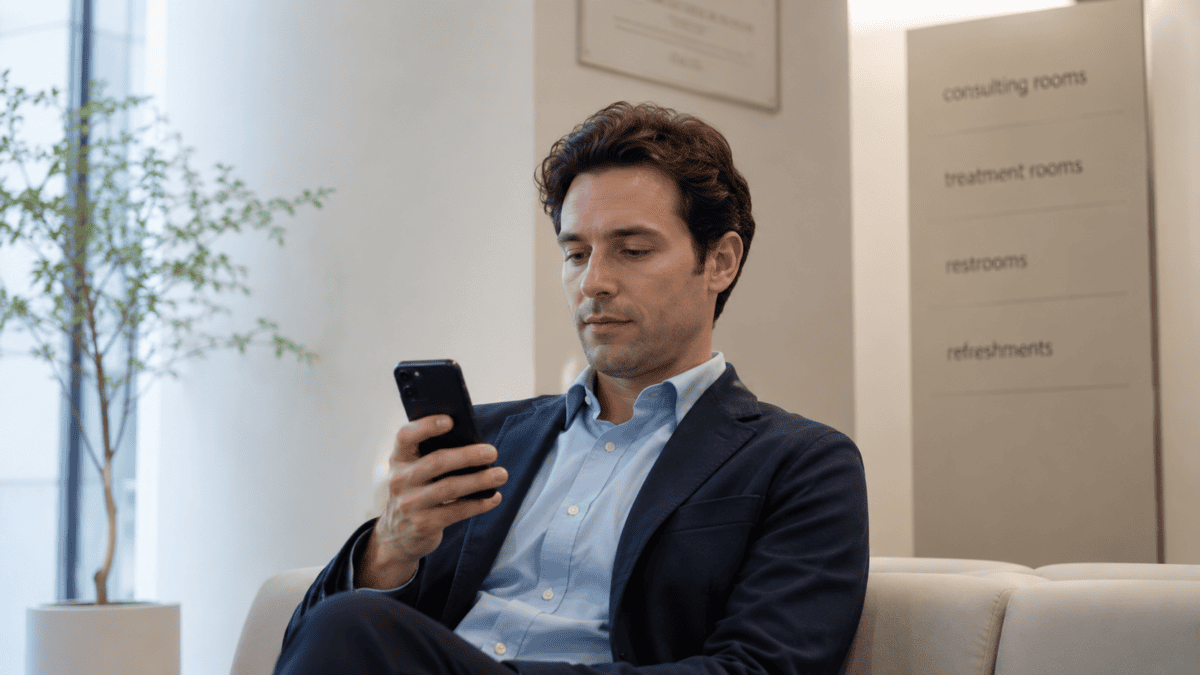 Man checks work emails in a clinic waiting room before non surgical skin treatments, quiet and discreet.