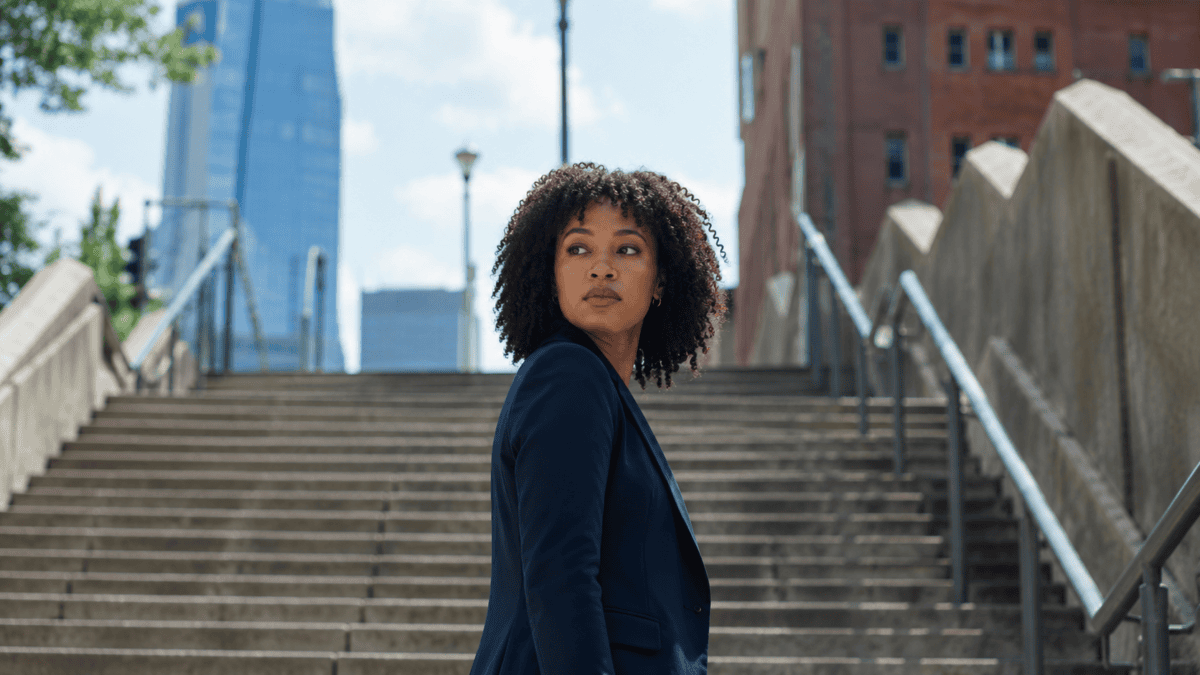 Woman stopped midway up a long staircase, looking back at how far she climbed — the sunk cost fallacy in action.